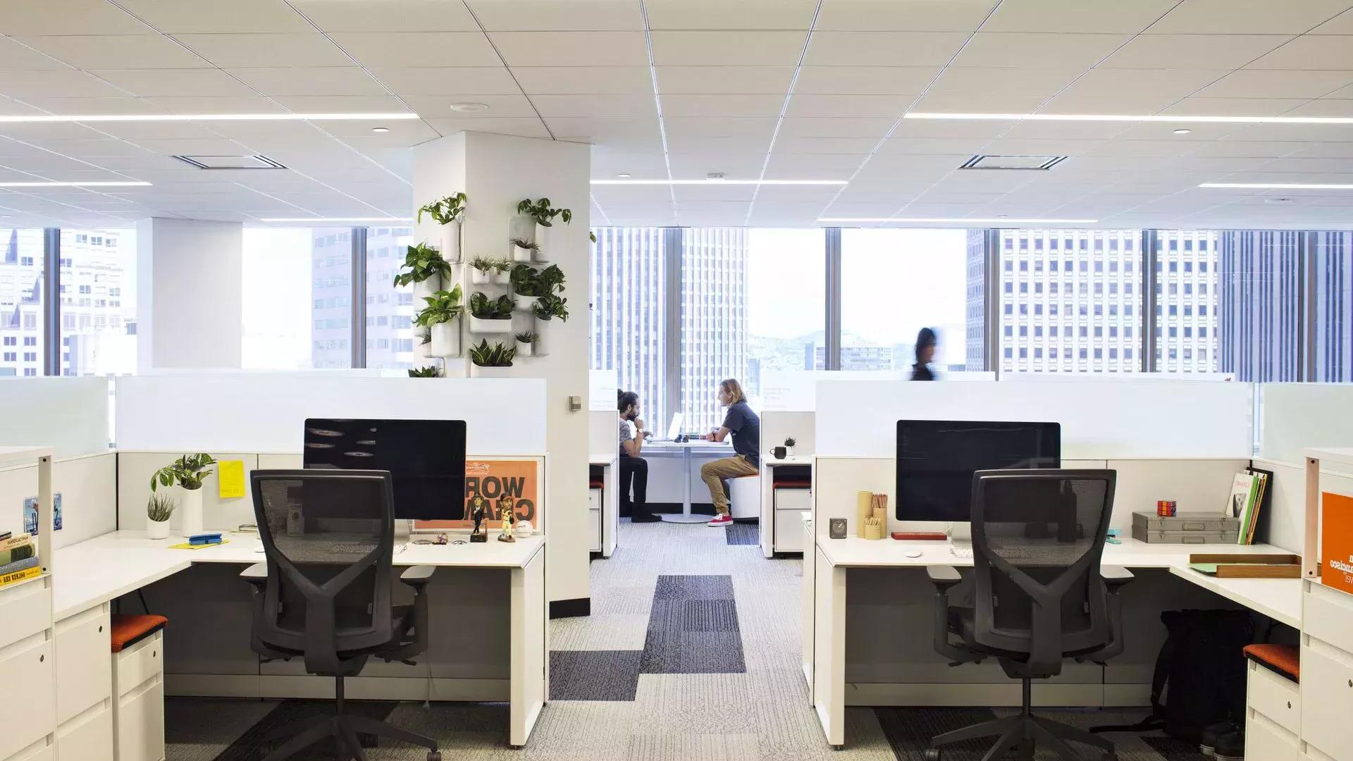 贝博体彩app一座办公楼的室内场景, 前景是办公室，两个人在大窗户前的一张桌子上工作.