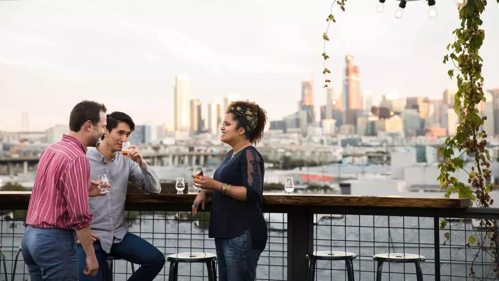 在贝博体彩app的Anchor Distilling屋顶上，三个人围坐在一张户外桌子旁, Califórnia.