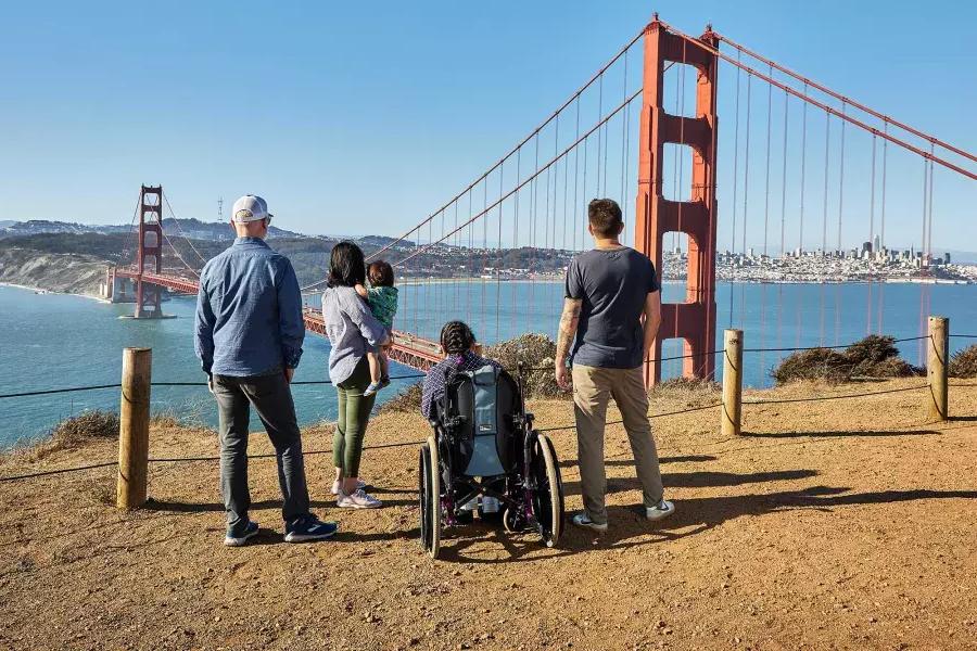 一群人, 包括一个坐轮椅的人, 从马林海角看金门大桥时，从后面可以看到它.