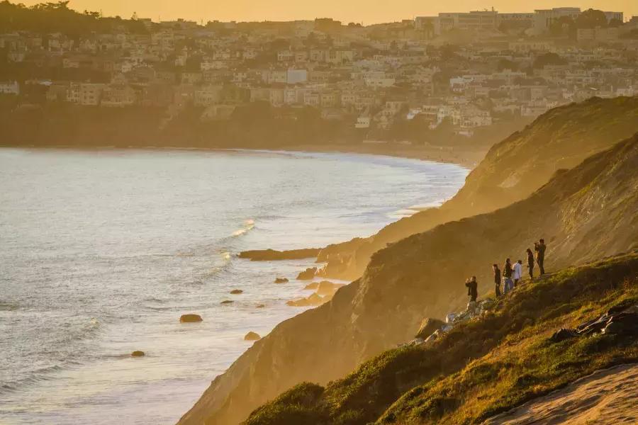 サンフランシスコのプレシディオで、海に面した崖の上に立って夕日を眺める人々のグループ。