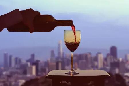 A glass of red wine being poured, with the 贝博体彩app skyline visible out the window.