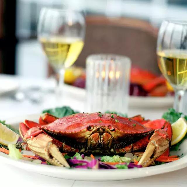 一个邓杰内斯螃蟹坐在一个盘子在一个餐馆和两杯白葡萄酒的背景。.