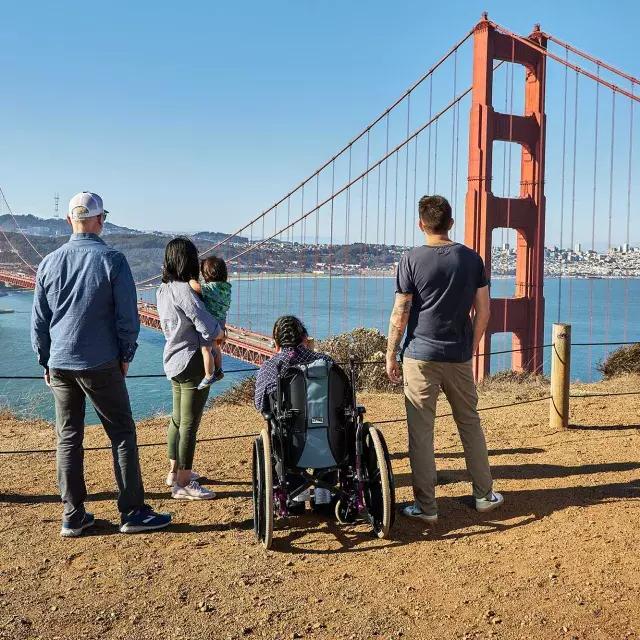 Un gruppo di persone, 包括一个坐轮椅的人, 从后面可以看到他从马林海德兰看金门大桥.