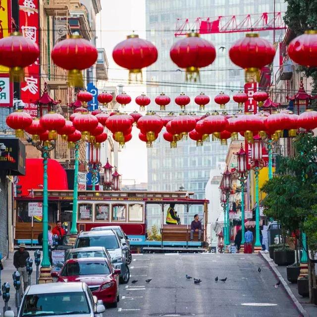 Une rue vallonnée du 邻里中国 de San Francisco est représentée avec des lanternes rouges suspendues et un tramway qui passe.